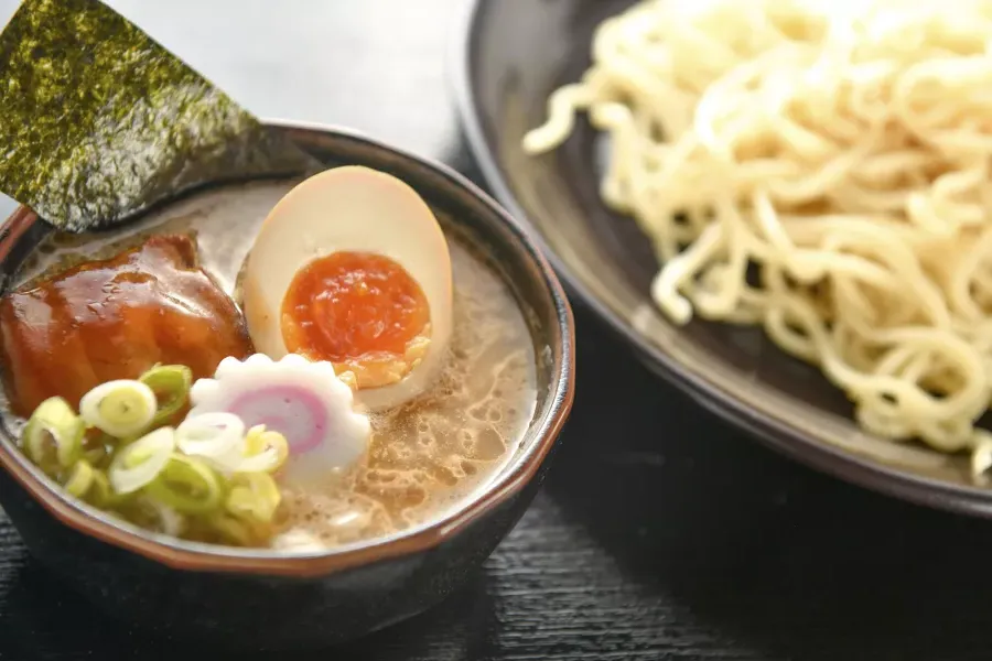 Close up shot of a bowl of noodles 和 a bowl of ramen soup with a poached egg, sliced in half.